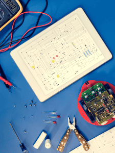 A tablet with a digital diagram rests on a blue mat with electrical equipment